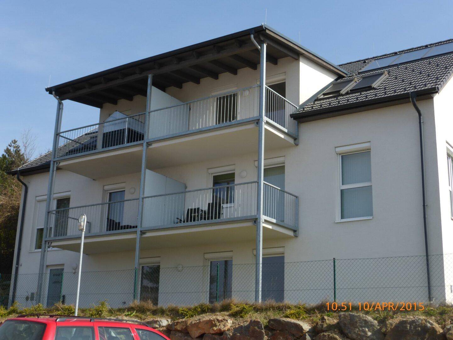 Modernes Mehrfamilienhaus mit mehreren Balkonen, Rollläden und Solaranlage auf dem Dach.