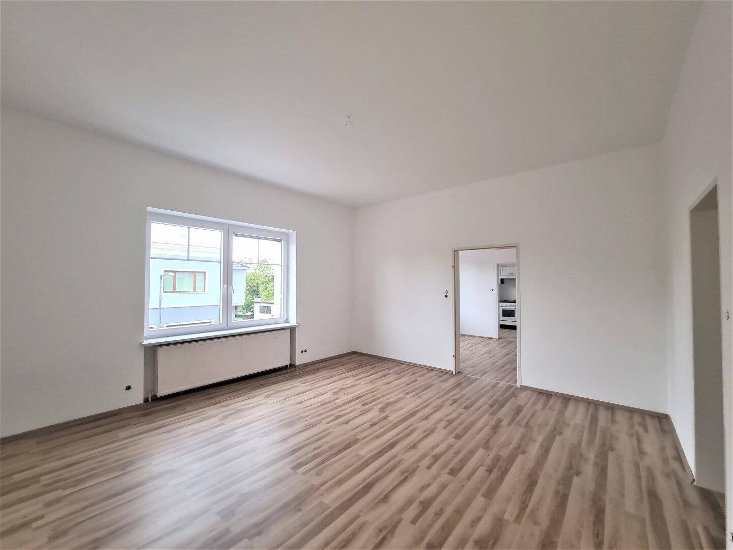 Leerer Raum mit Laminatboden und einem Durchgang, der zu einem weiteren Zimmer oder der Küche führt.