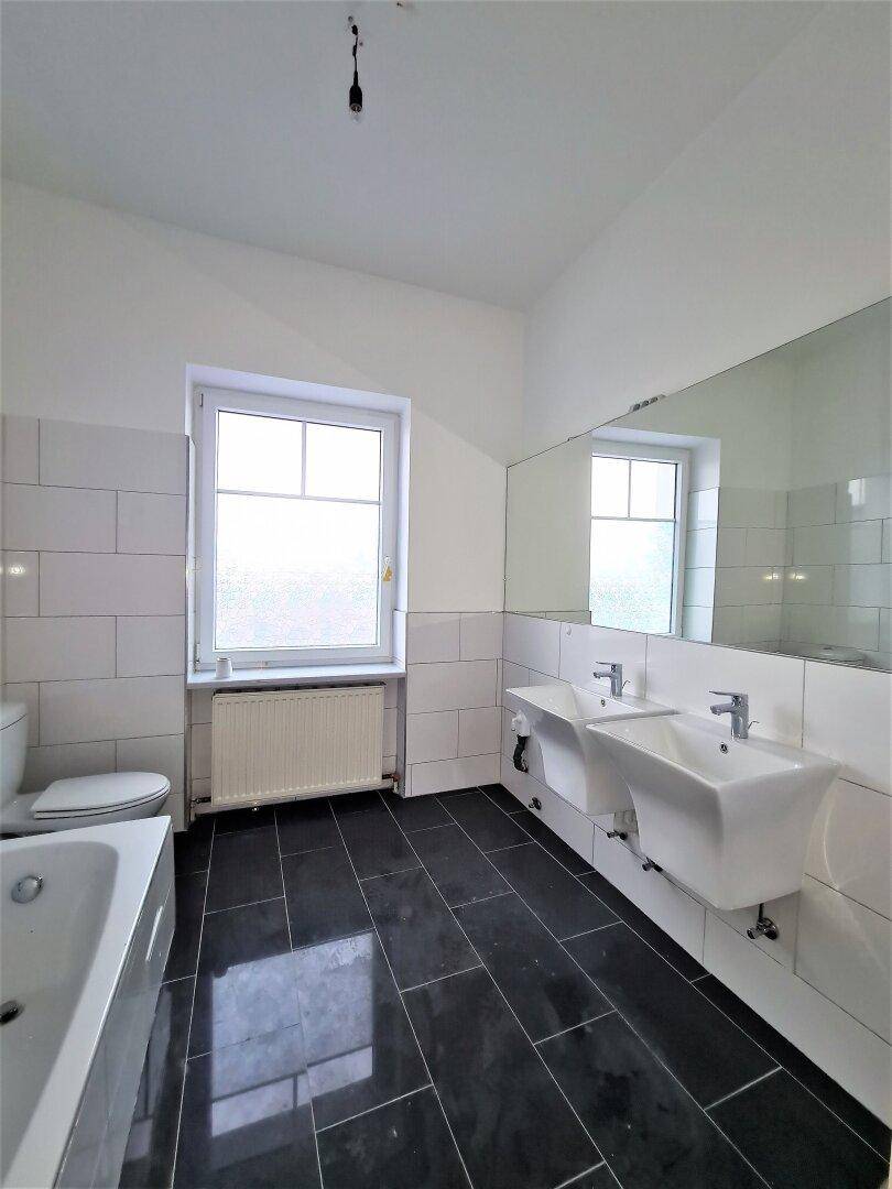Modernes Badezimmer mit Badewanne, Doppelwaschbecken, WC und dunklen Bodenfliesen.
