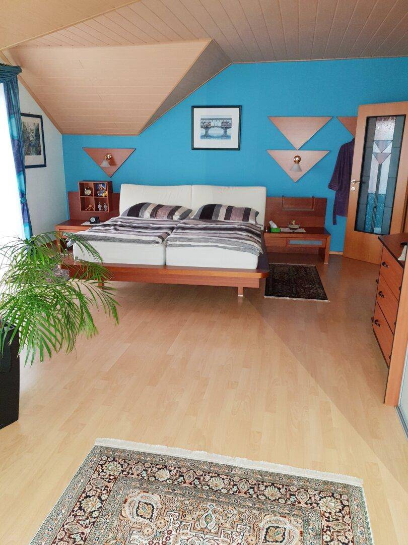 Schlafzimmer mit blauen Wänden, Holzboden, Doppelbett und Dachschrägen.