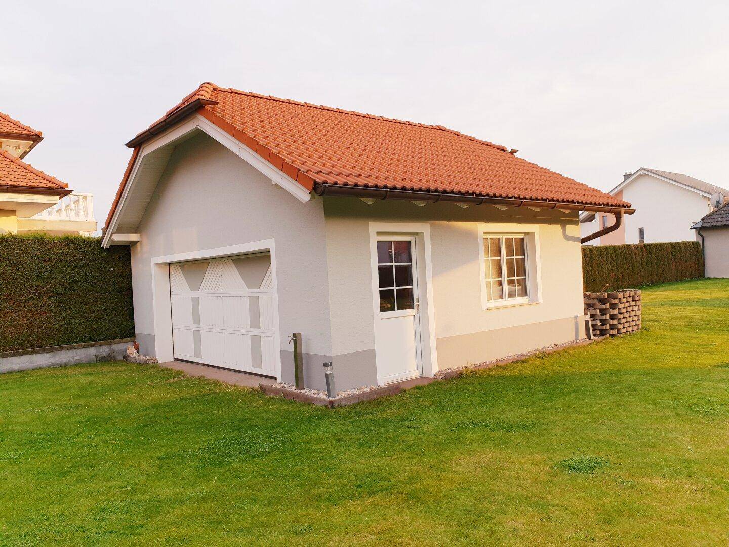 Freistehende Garage mit Satteldach und weißem Tor, umgeben von einer grünen Rasenfläche.
