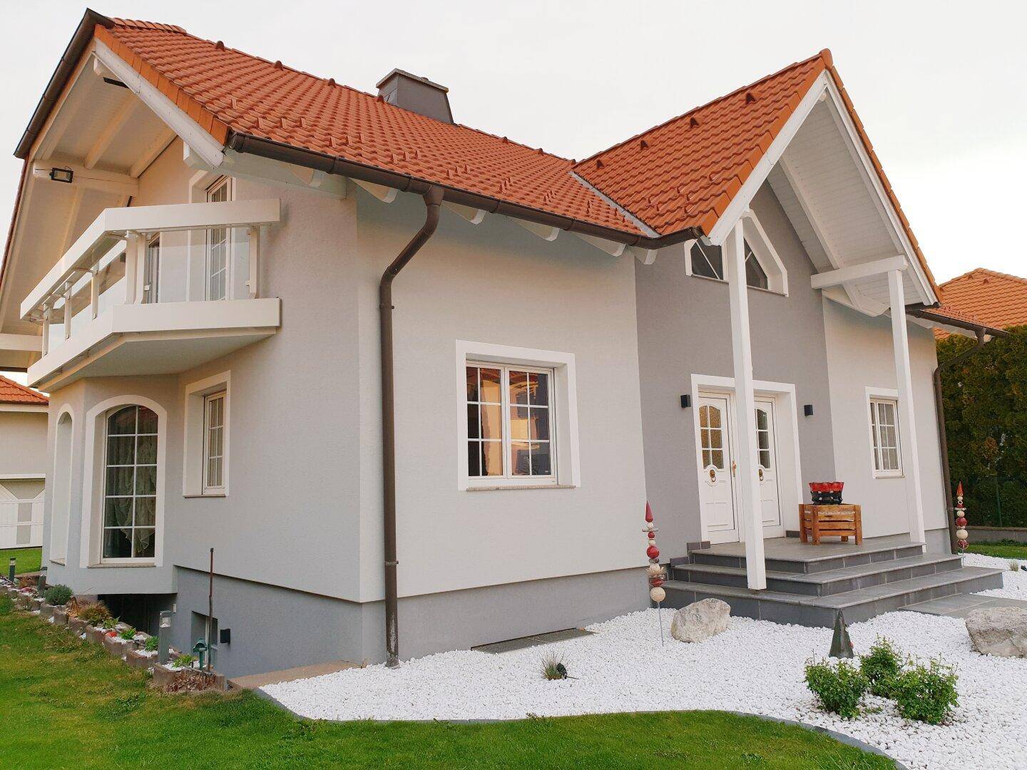 Modernes Einfamilienhaus mit Satteldach, Balkon und heller Fassade, umgeben von einem gepflegten Garten.