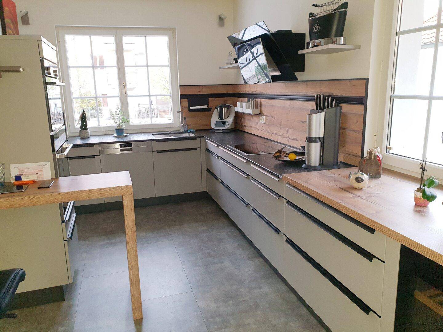 Moderne Küche mit hellgrauen Fronten, Holzakzenten und Fenster für Tageslicht.