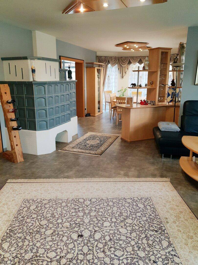 Geräumiges Wohnzimmer mit großem Kachelofen, Teppichen und Übergang zum Essbereich.