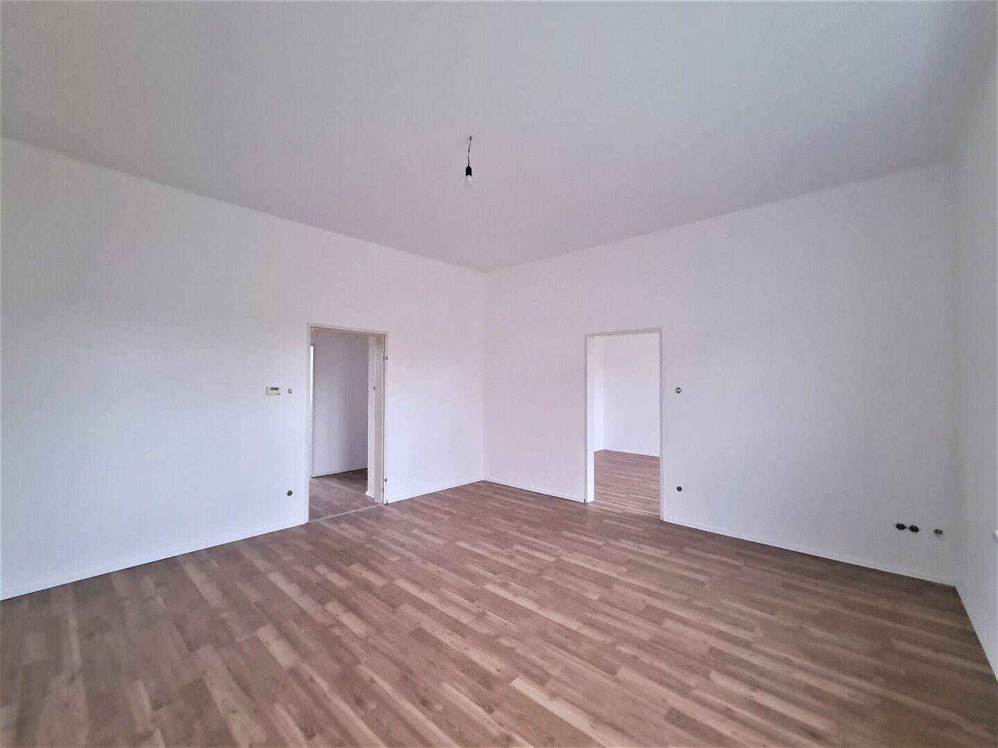 Geräumiger, heller Raum mit Laminatboden und zwei Türen, die zu angrenzenden Zimmern führen.