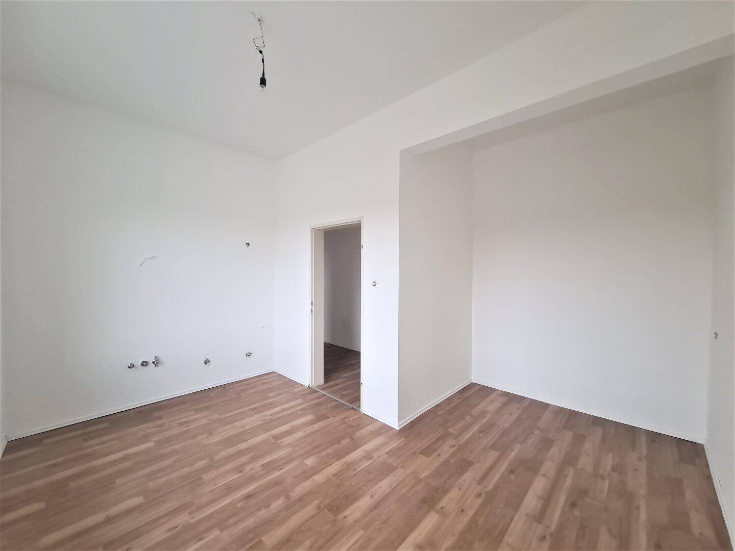 Leerer Raum mit Laminatboden und einem Durchgang zu einem weiteren Zimmer, ideal für flexible Nutzung.