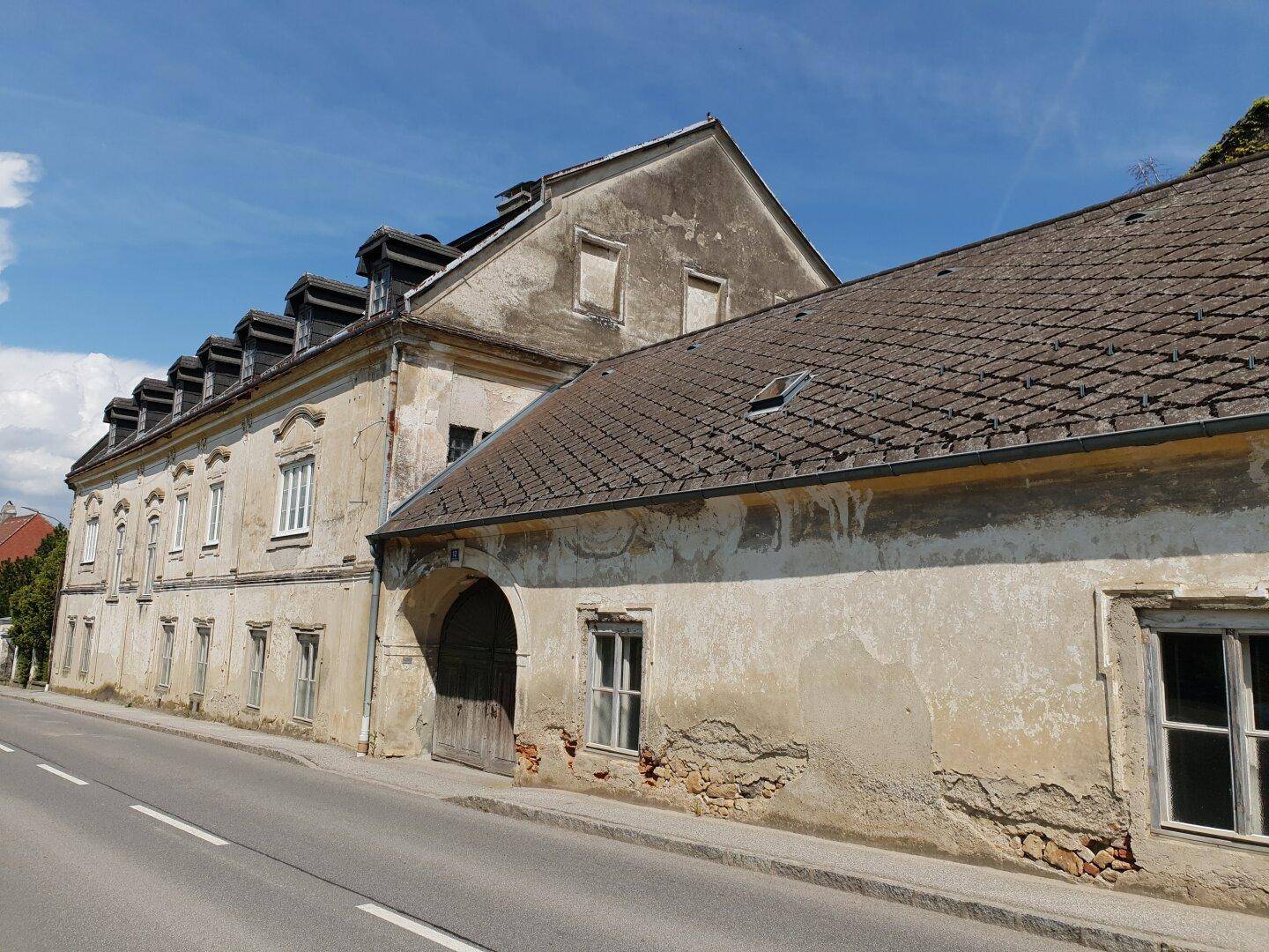 Altes Gebäude mit markanter Fassade, Satteldach und großem Torbogen direkt an der Straße.