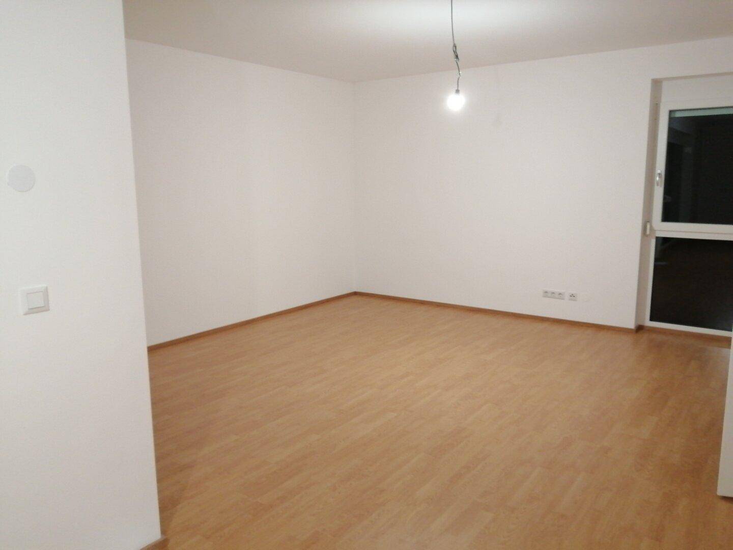 Leerer Raum mit hellem Laminatboden und einem Fenster, bereit für die individuelle Gestaltung.