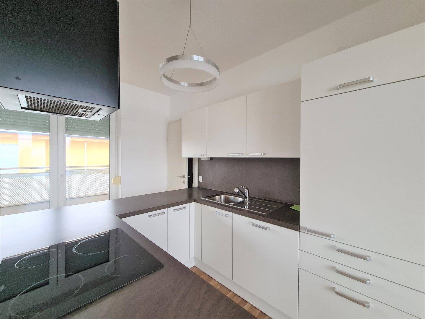 Moderne Einbauküche mit weißen Schränken, dunkler Arbeitsplatte und Induktionskochfeld.