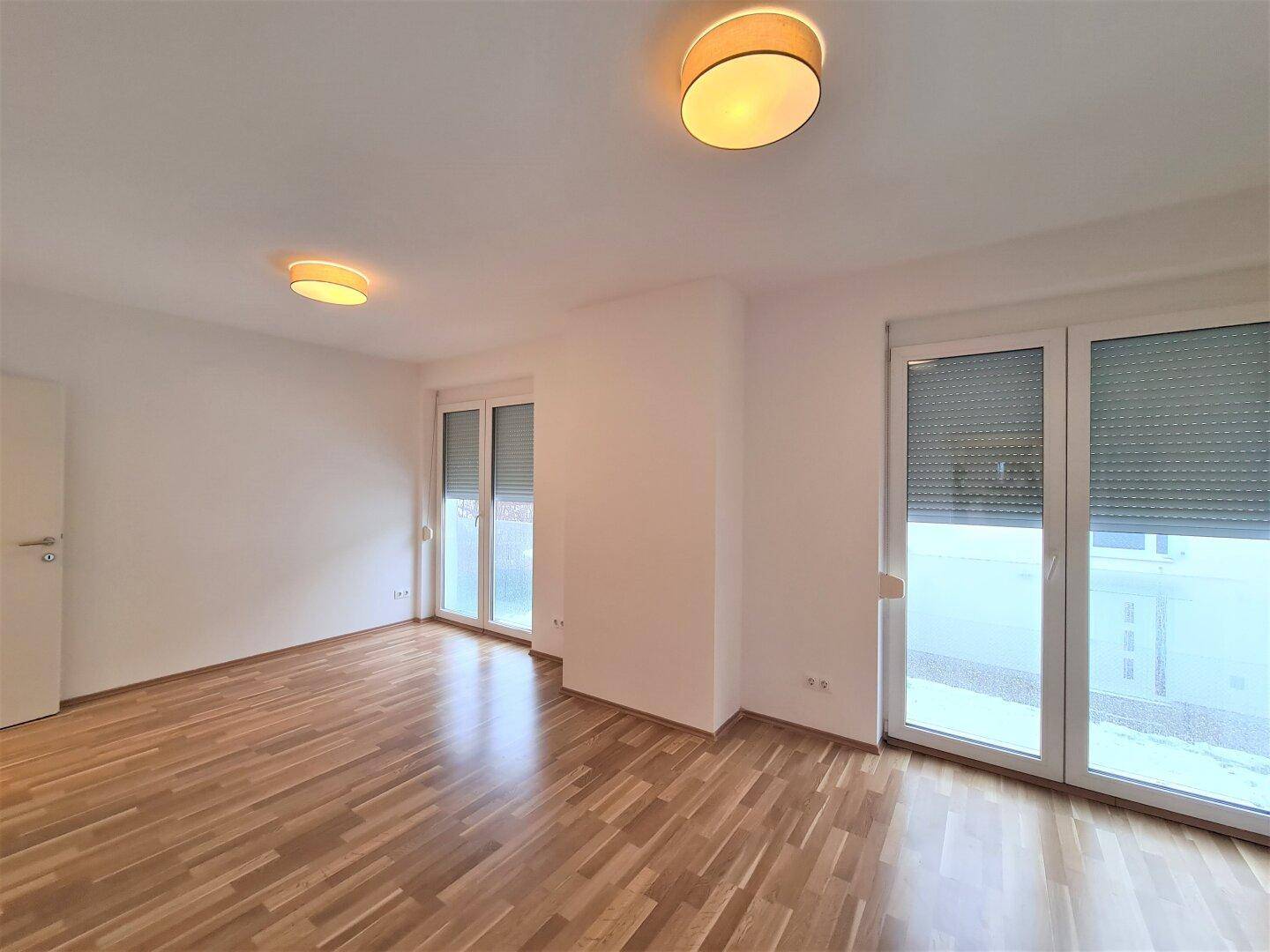 Geräumiges Schlafzimmer mit Parkettboden und großen Fenstern mit Zugang zum Balkon.