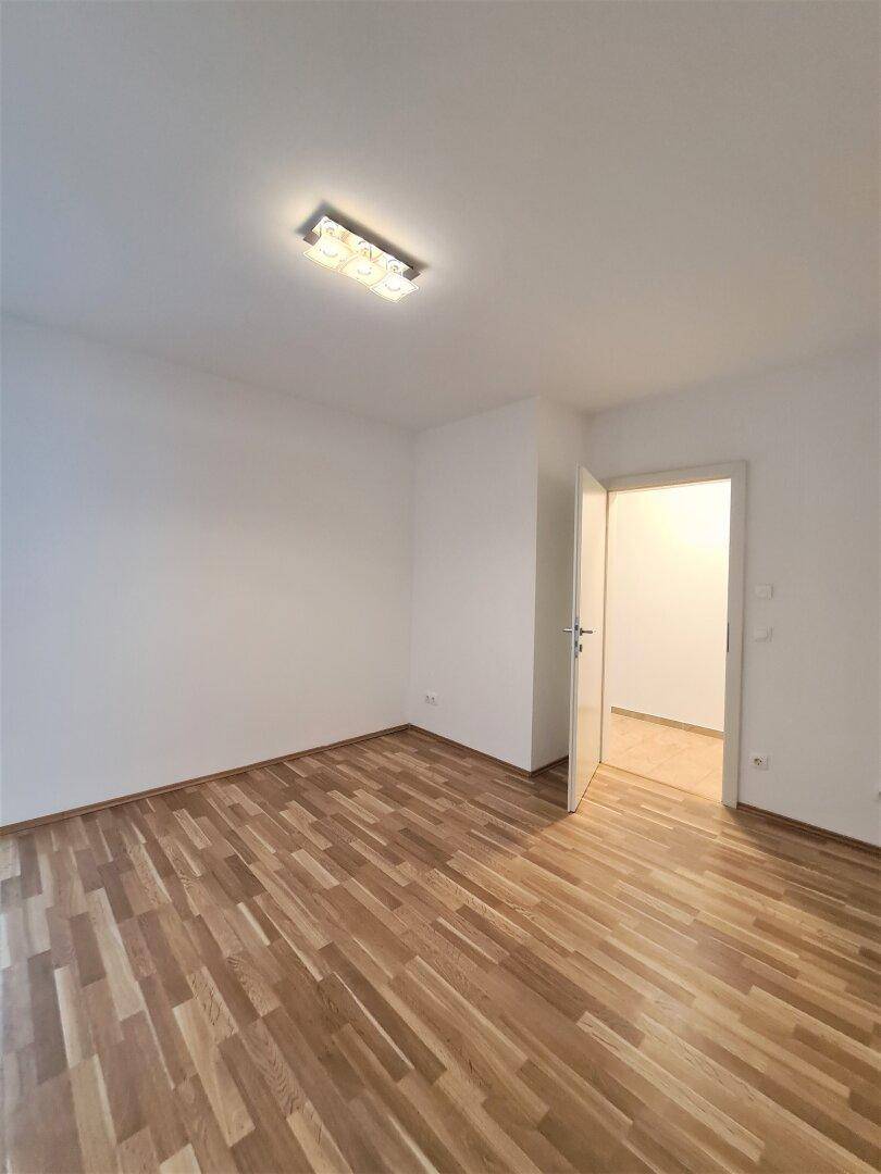 Leeres Zimmer mit hellem Parkettboden und Zugang zu einem weiteren Raum.