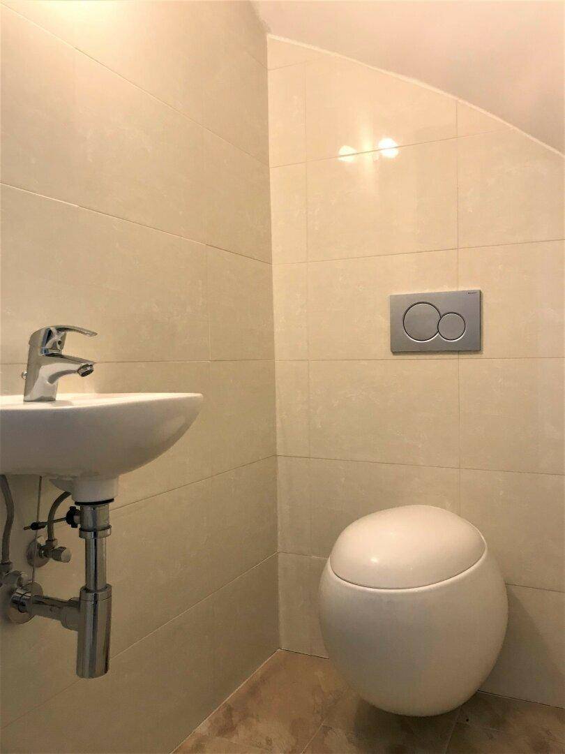 Kleines Gäste-WC mit Wand-WC, Waschbecken und hellen Fliesen.