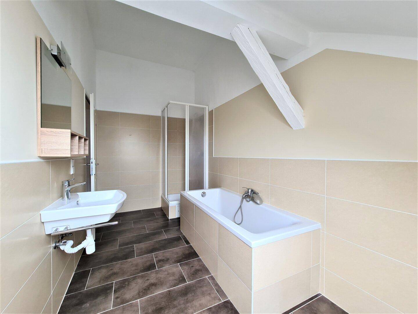 Modernes Badezimmer mit Badewanne, Duschkabine und Waschbecken unter einer Dachschräge.