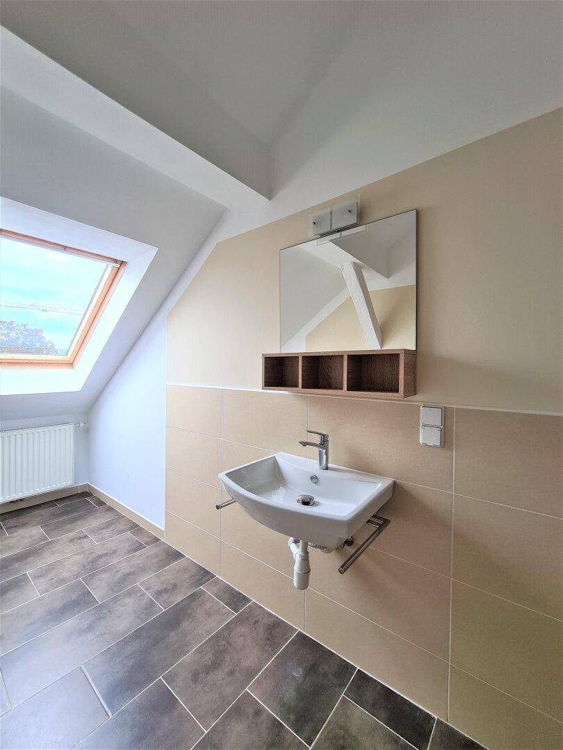 Badezimmer im Dachgeschoss mit Waschbecken, beigefarbenen Fliesen und einem Dachfenster.