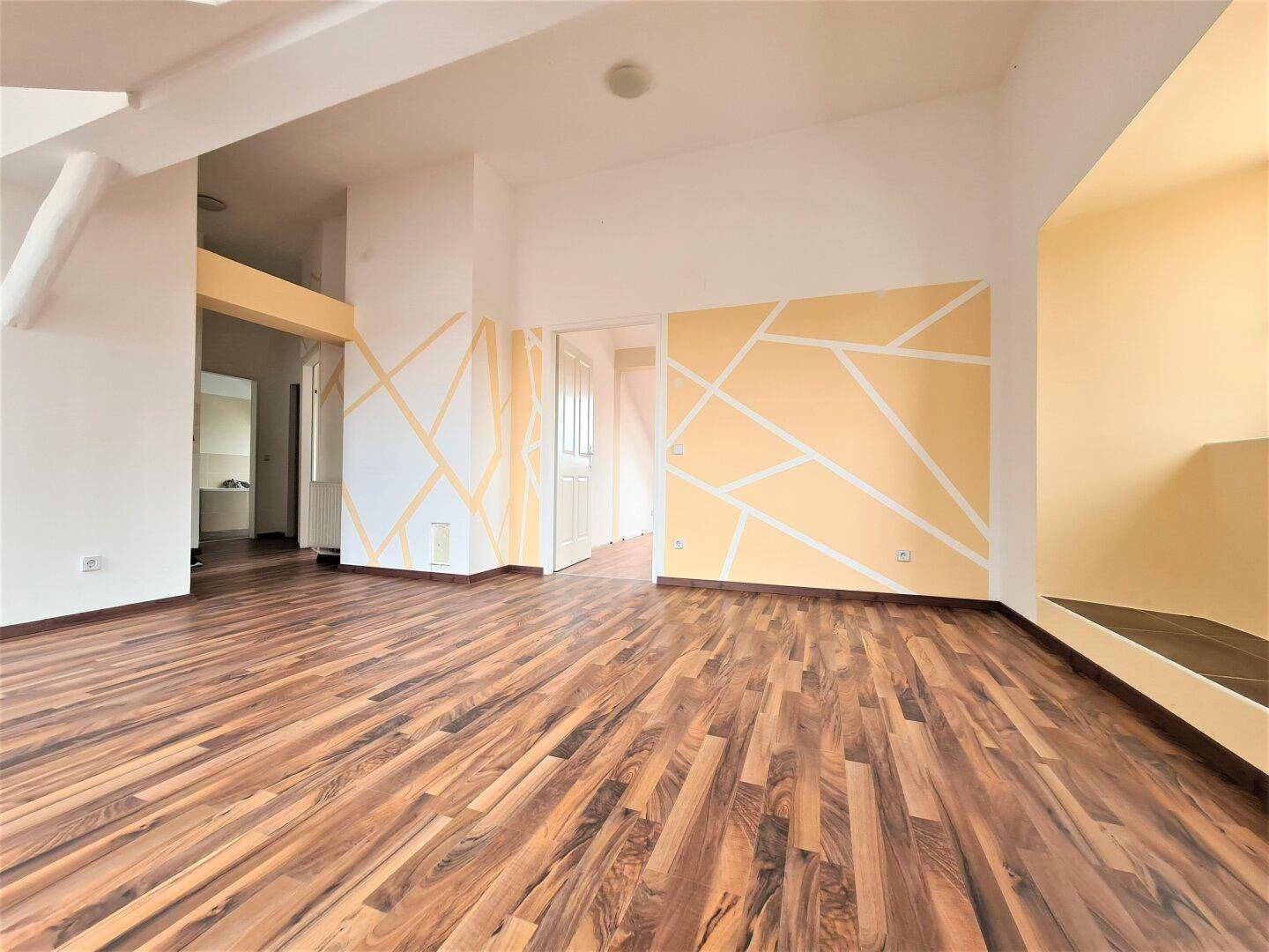 Großer, heller Raum mit Laminatboden und Dachschrägen, verziert mit modernen geometrischen Wandmustern.