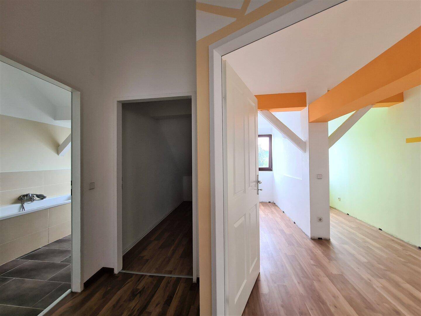 Übergangsbereich mit Laminatboden, der zu einem Badezimmer und einem weiteren Raum mit Holzbalken führt.
