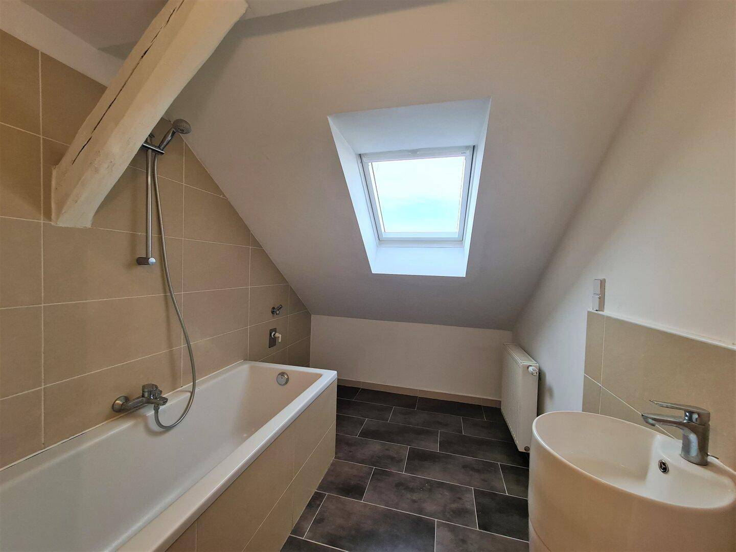 Badezimmer im Dachgeschoss mit Badewanne, Waschbecken, beigefarbenen Fliesen und Dachfenster.