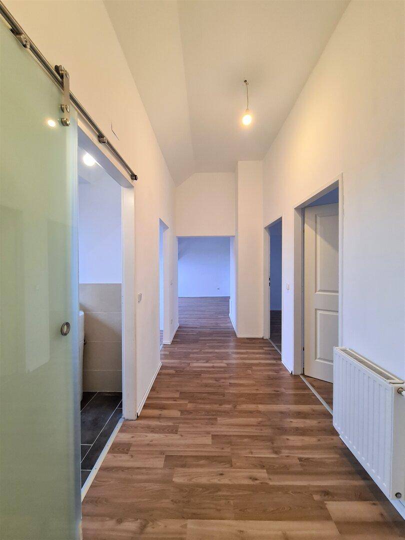 Heller Flur mit Laminatboden, weiß gestrichenen Wänden und einer modernen Glasschiebetür.