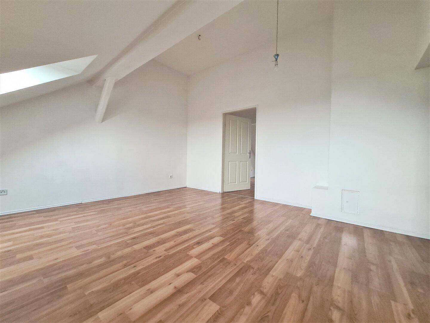 Geräumiger, leerer Raum mit Laminatboden, weißen Wänden und einer Dachschräge.