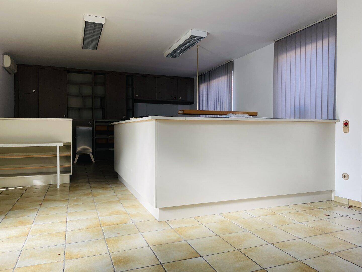 Bürointerieur mit langer Theke, dunklen Einbauschränken und hellen Fliesen, bereit für die Nutzung.