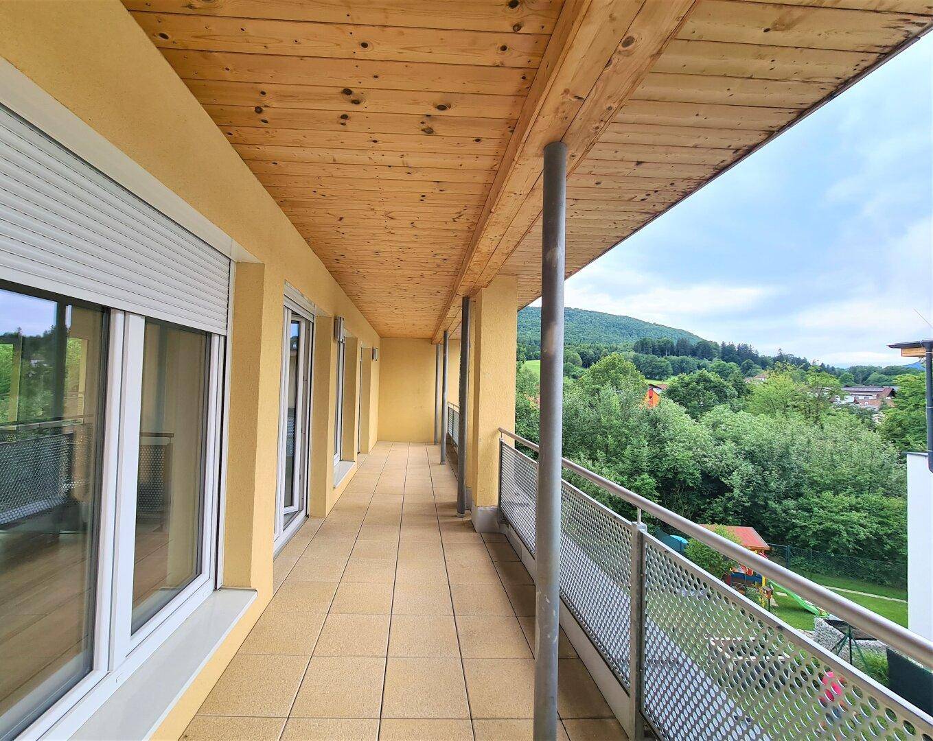 Geräumiger überdachter Balkon mit Fliesenboden und weitem Blick auf die grüne Landschaft.