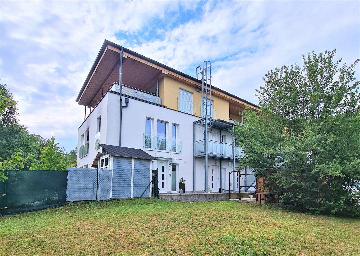 Modernes Wohngebäude mit Gartenfläche, Außentreppe und umgebender Natur.