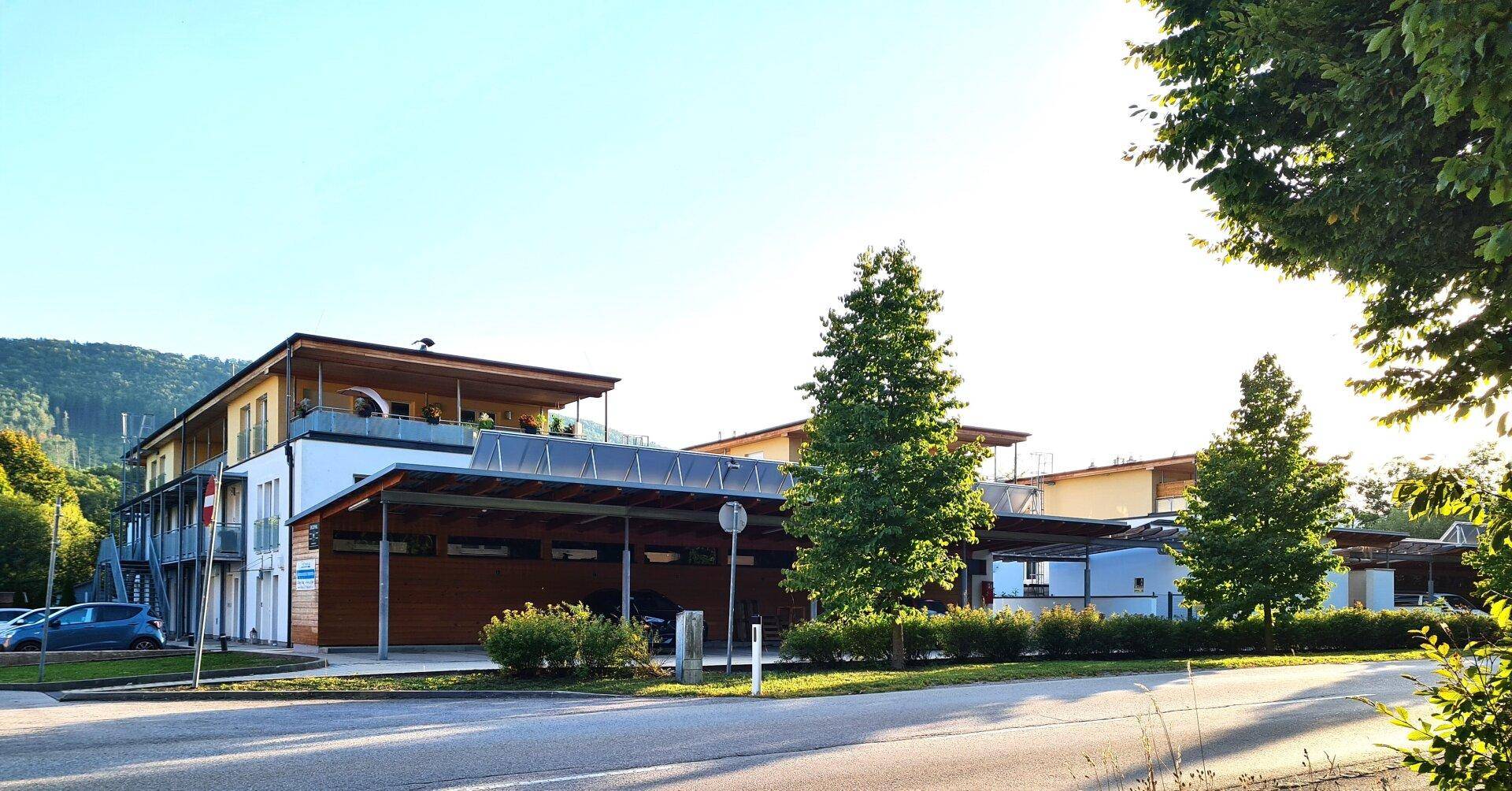 Modernes Wohngebäude mit Carports und begrüntem Außenbereich unter blauem Himmel.