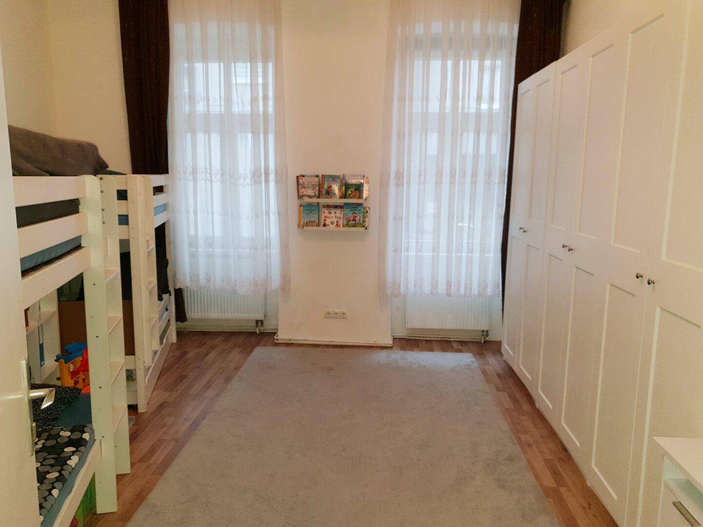 Helles Kinderzimmer mit Etagenbetten, einem großen weißen Kleiderschrank und Laminatboden.