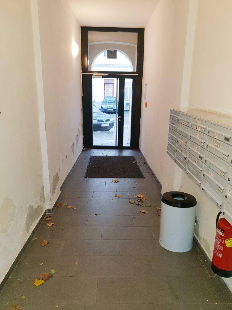 Eingangsbereich des Gebäudes mit Briefkästen, Feuerlöscher und Blick zur Straße.