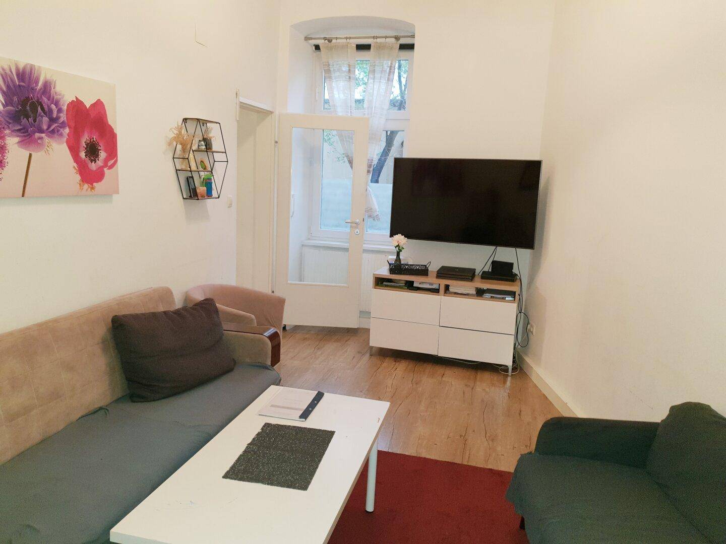 Gemütliches Wohnzimmer mit Sofa, Fernseher und Zugang zu einem kleinen Außenbereich.