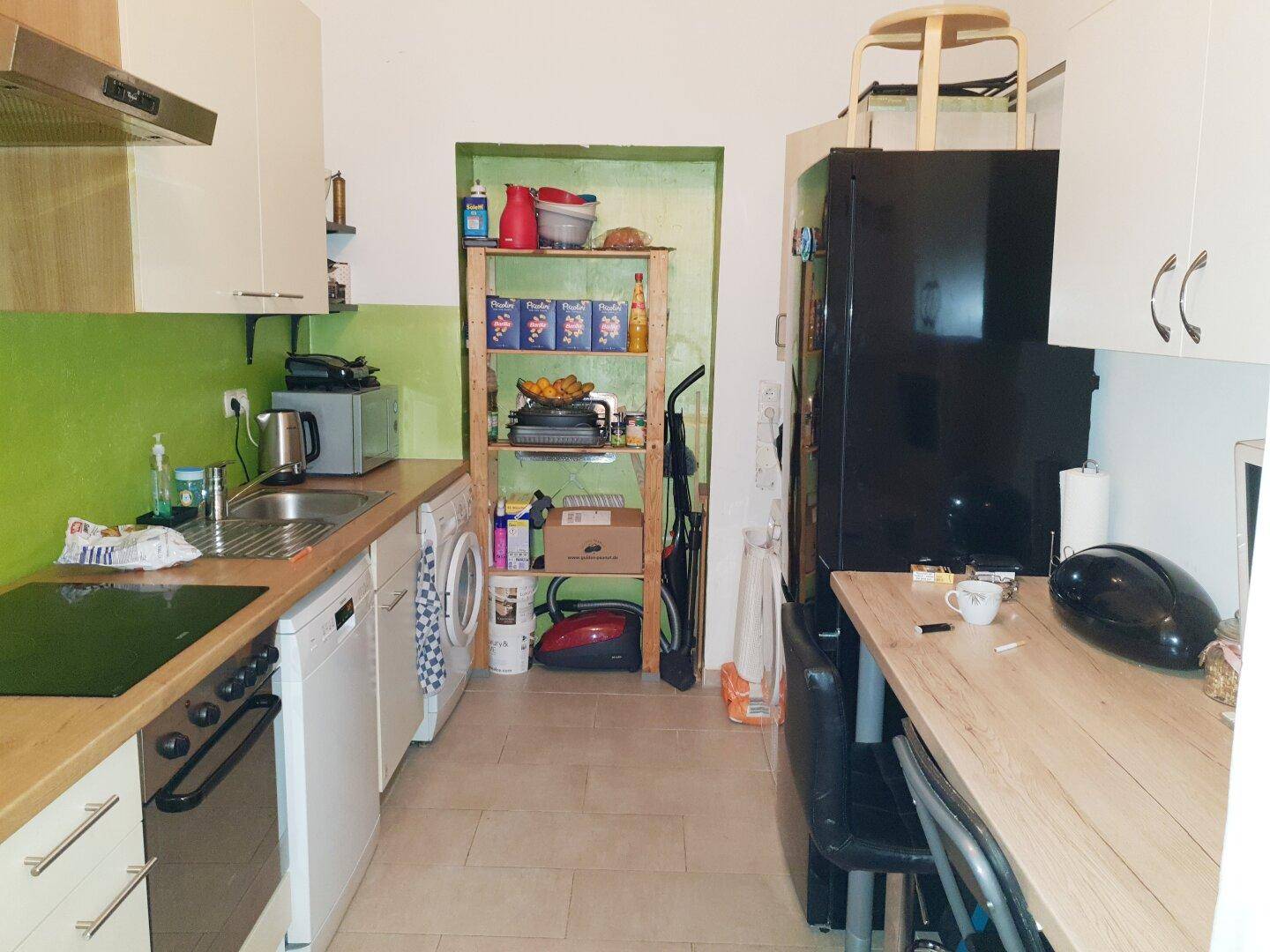 Kleine, funktionale Küche mit grüner Wand, Holztheke und integrierten Haushaltsgeräten.
