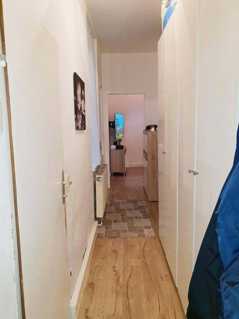 Heller Flur mit Laminatboden und weißen Schränken, der zu weiteren Räumen führt.