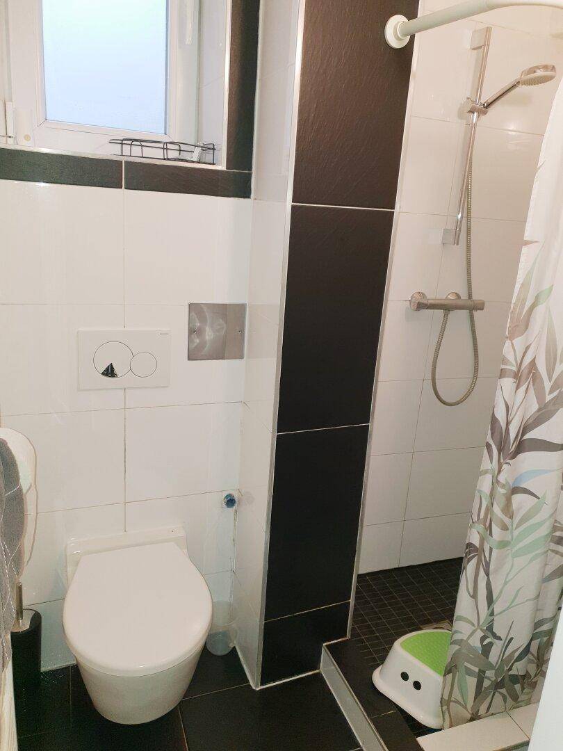 Modernes Badezimmer mit Dusche, wandhängendem WC und schwarz-weißen Fliesen.