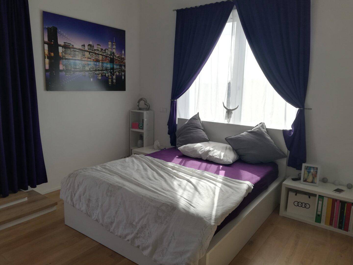 Gemütliches Schlafzimmer mit Doppelbett, lila Vorhängen und einem Bild an der Wand.