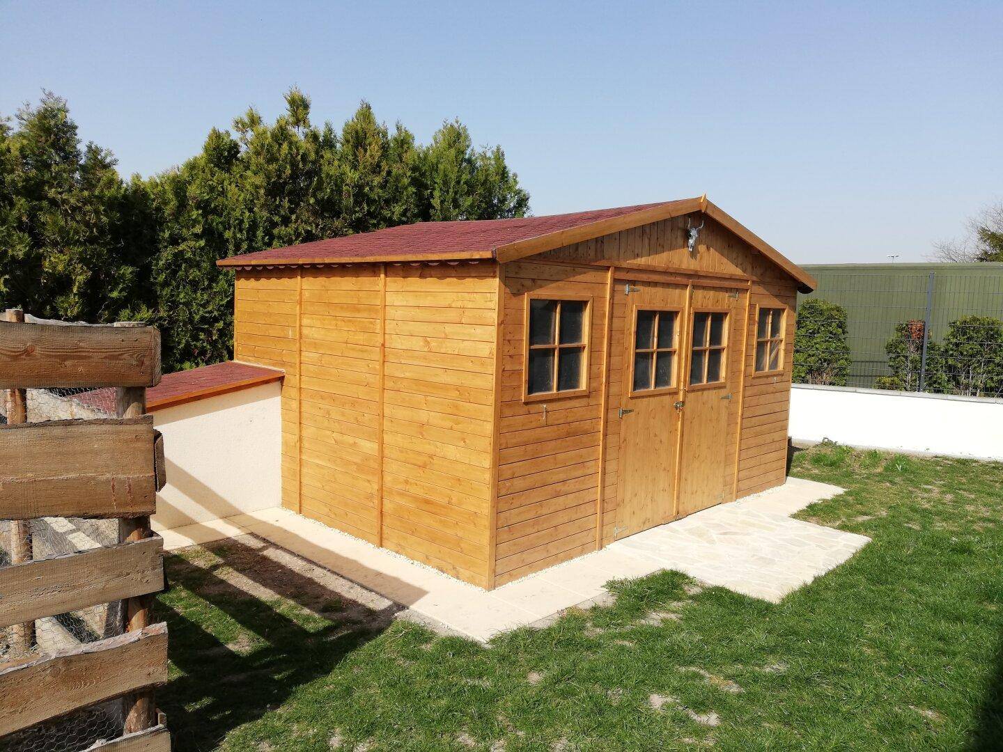 Robuster Holzschuppen im Garten mit rotem Dach und mehreren Fenstern.
