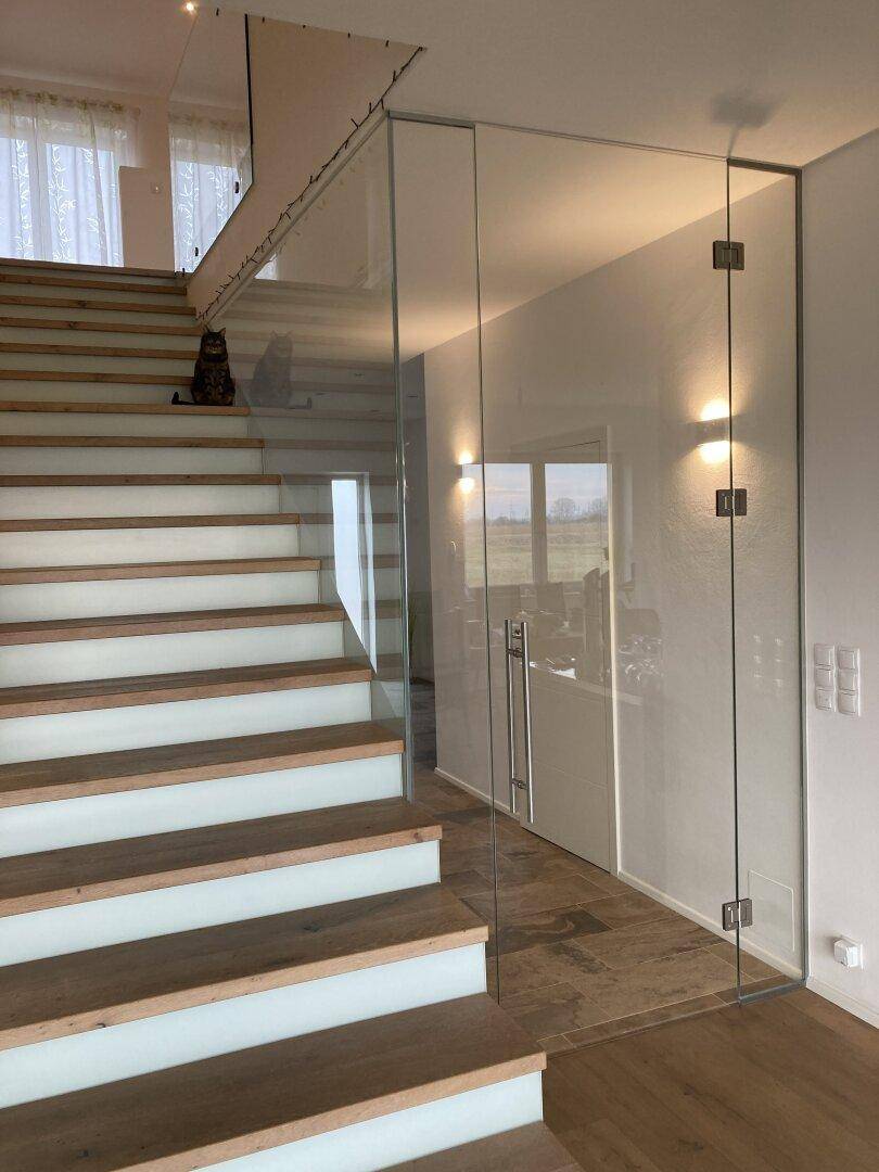 Moderne Treppe mit Holzstufen und eleganter Glasbrüstung, die die Etagen verbindet.