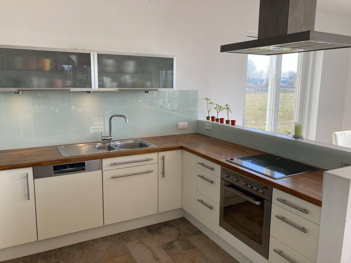 Helle Küche mit Induktionskochfeld, Backofen, Spüle und Fenster mit Blick ins Grüne.