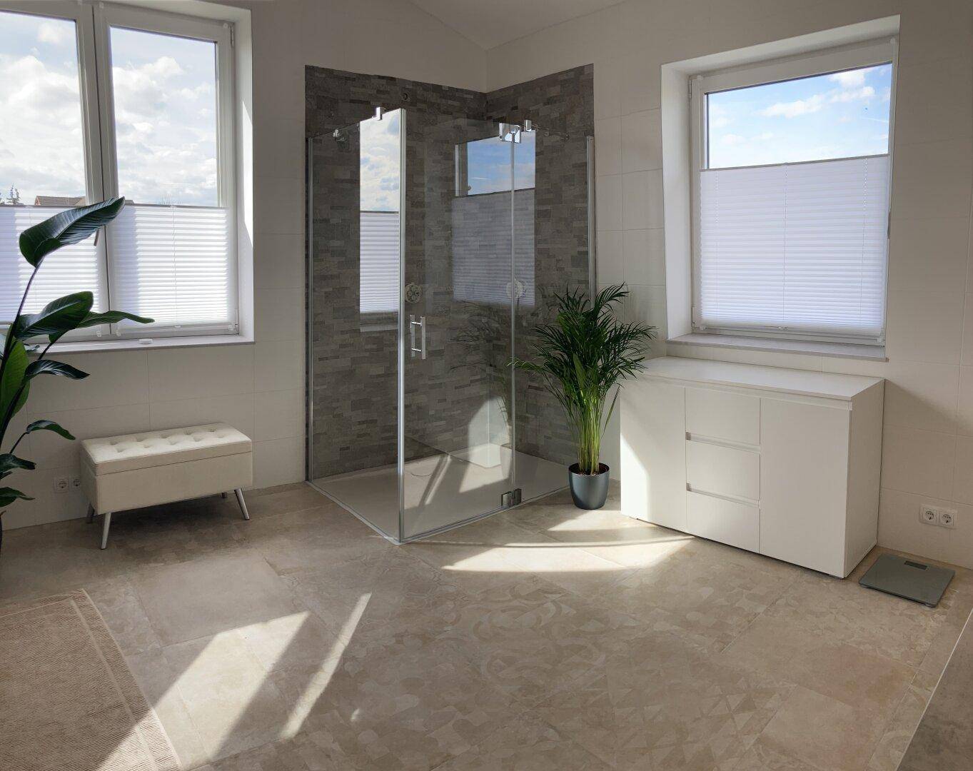 Modernes Badezimmer mit großer begehbarer Dusche, zwei Fenstern und Pflanzen.