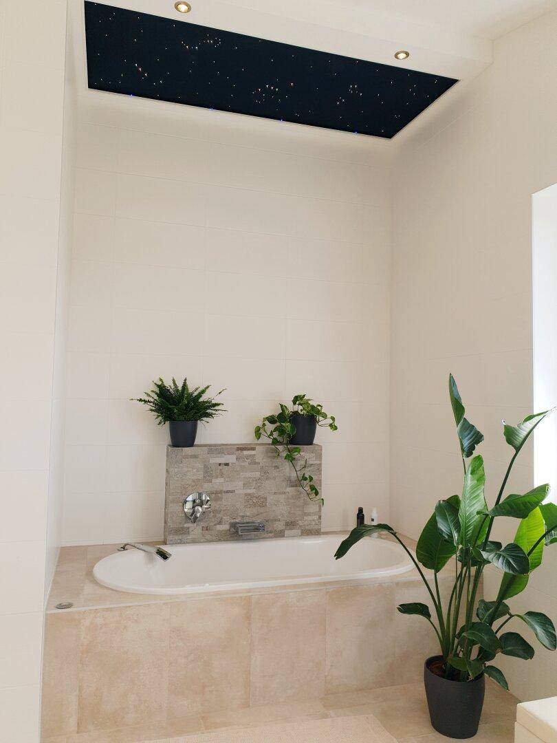 Entspannendes Badezimmer mit Badewanne, Pflanzen und einer Decke mit Sternenhimmel-Effekt.