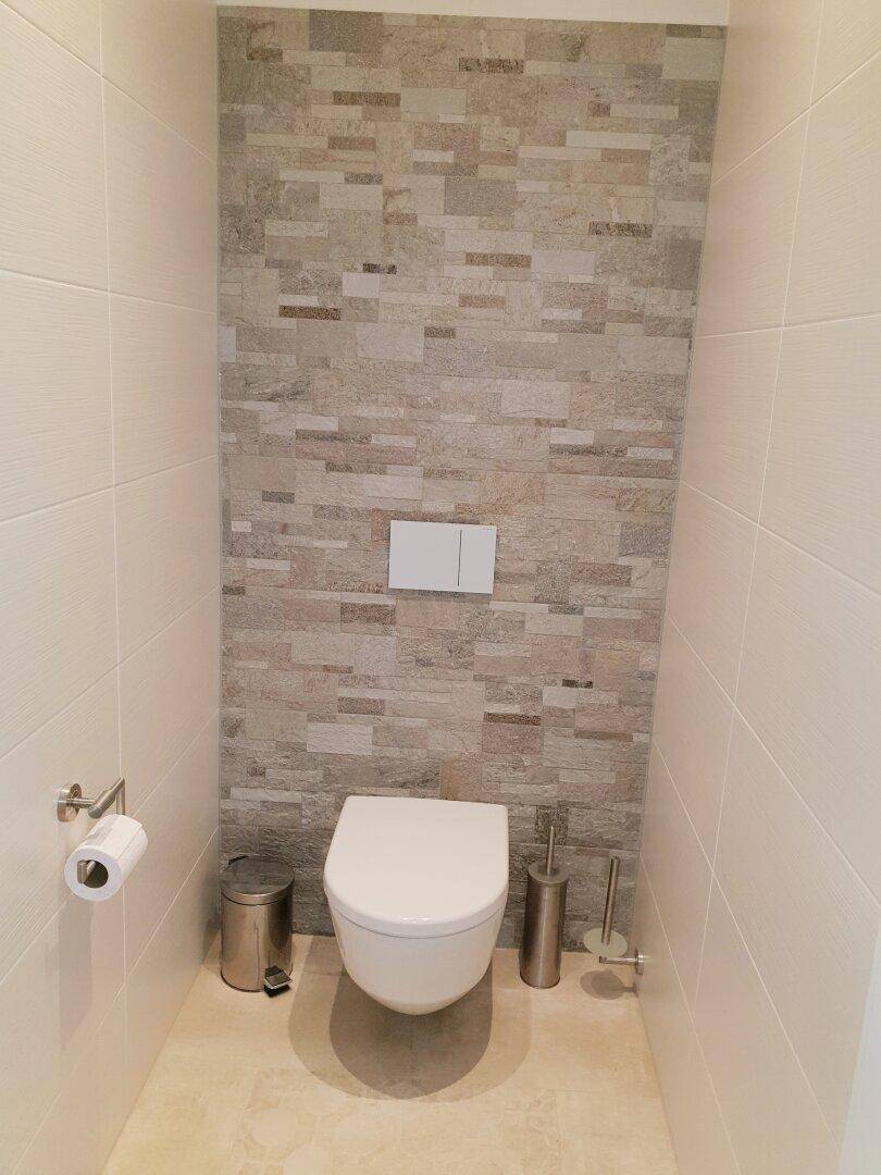 Modernes WC mit wandhängender Toilette und stilvoller Steinoptik-Fliesenwand.