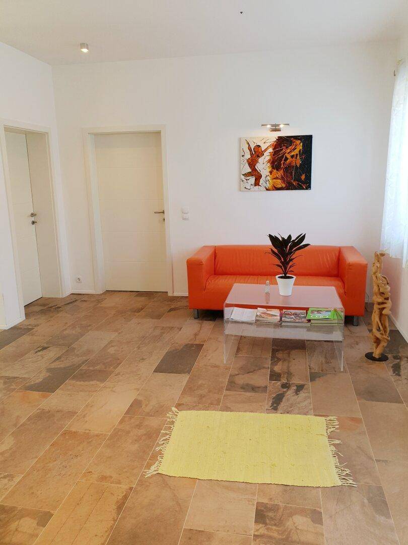 Heller Eingangsbereich mit Fliesenboden, orangefarbenem Sofa und moderner Kunst an der Wand.