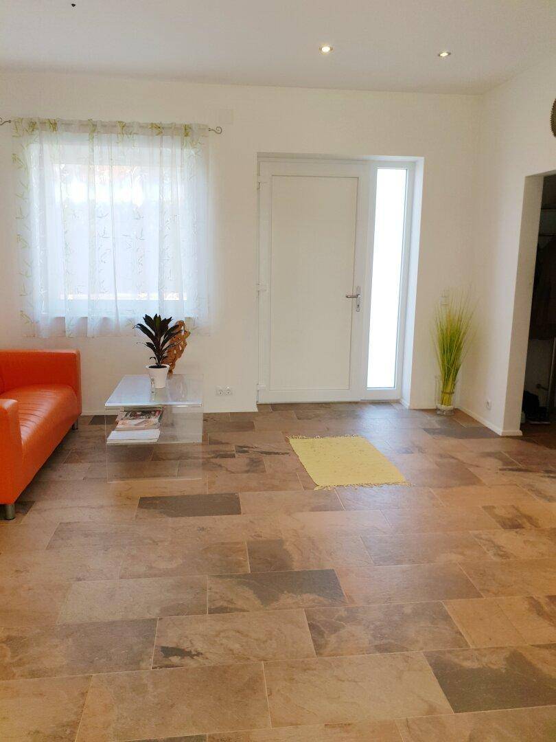 Eingangsbereich mit Fliesenboden, kleiner orangefarbener Couch und Fenster mit Vorhang.