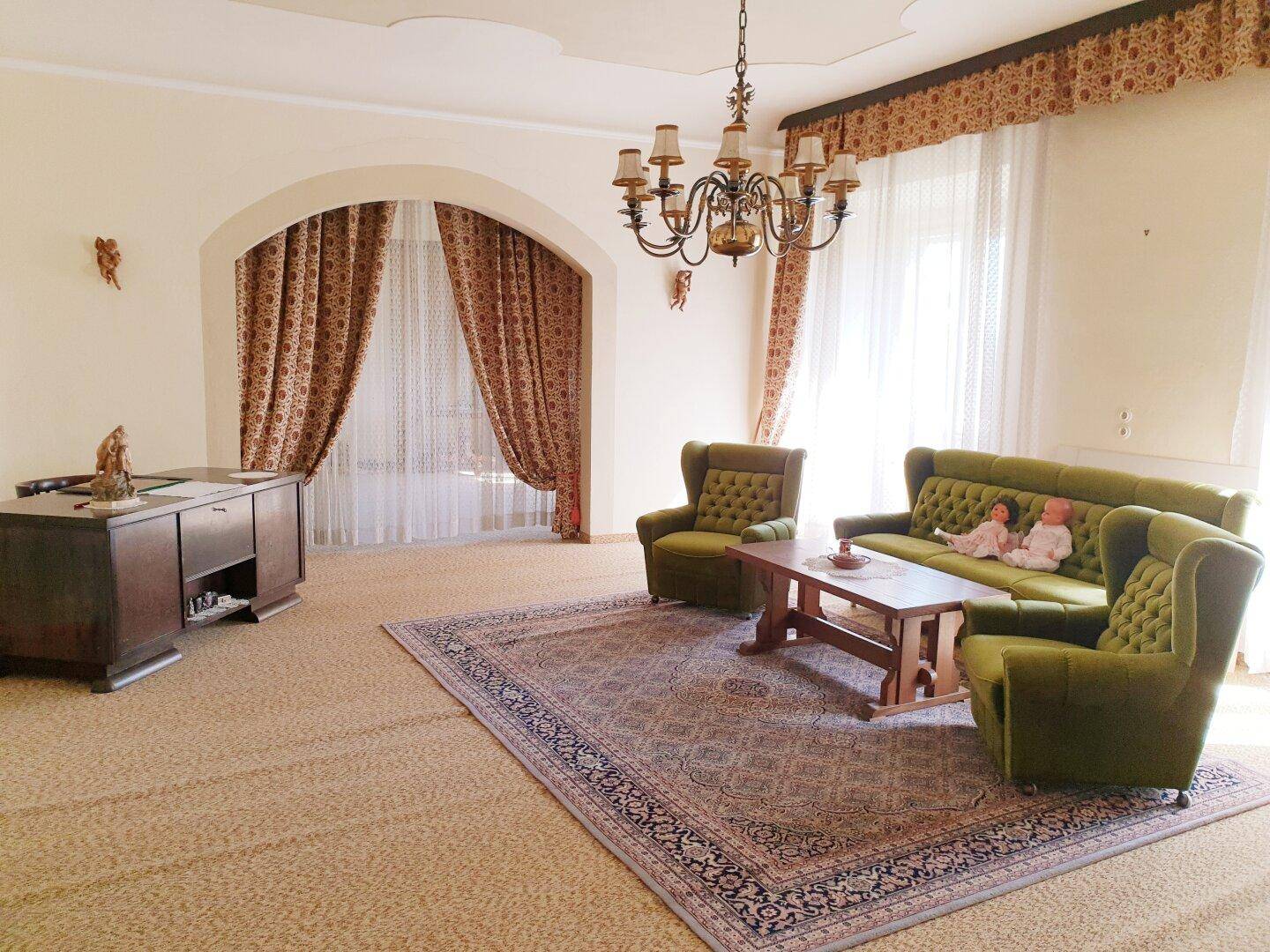 Geräumiges Wohnzimmer mit traditionellen Möbeln, Teppichboden und Kronleuchter.