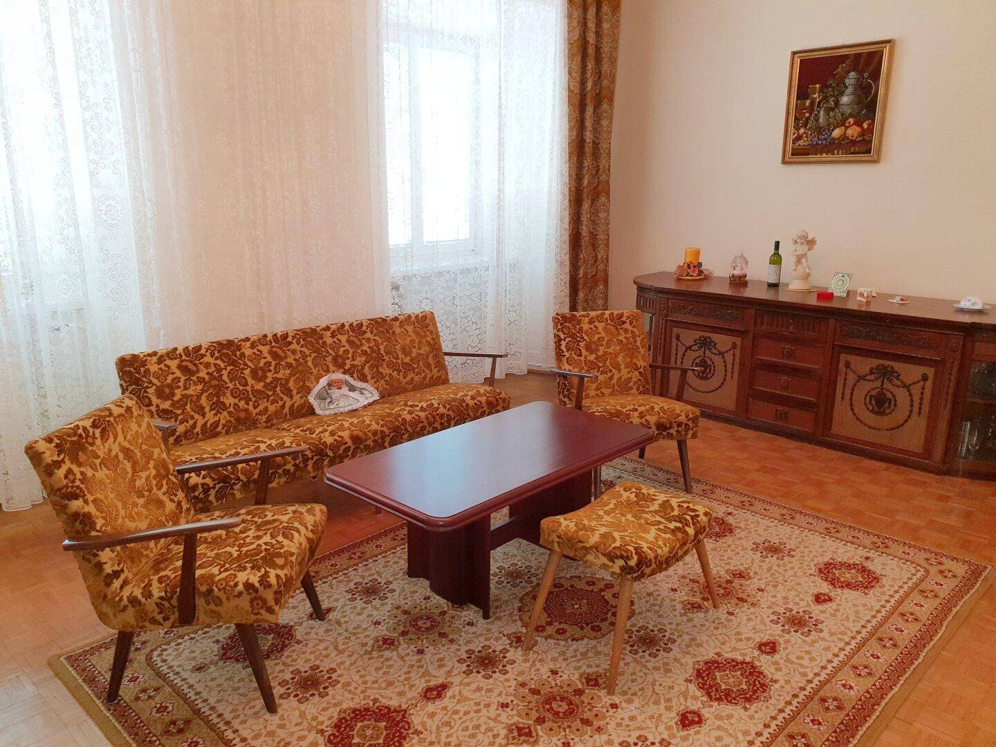 Wohnzimmer mit gemusterten Vintage-Möbeln, Holzboden und einem traditionellen Teppich.