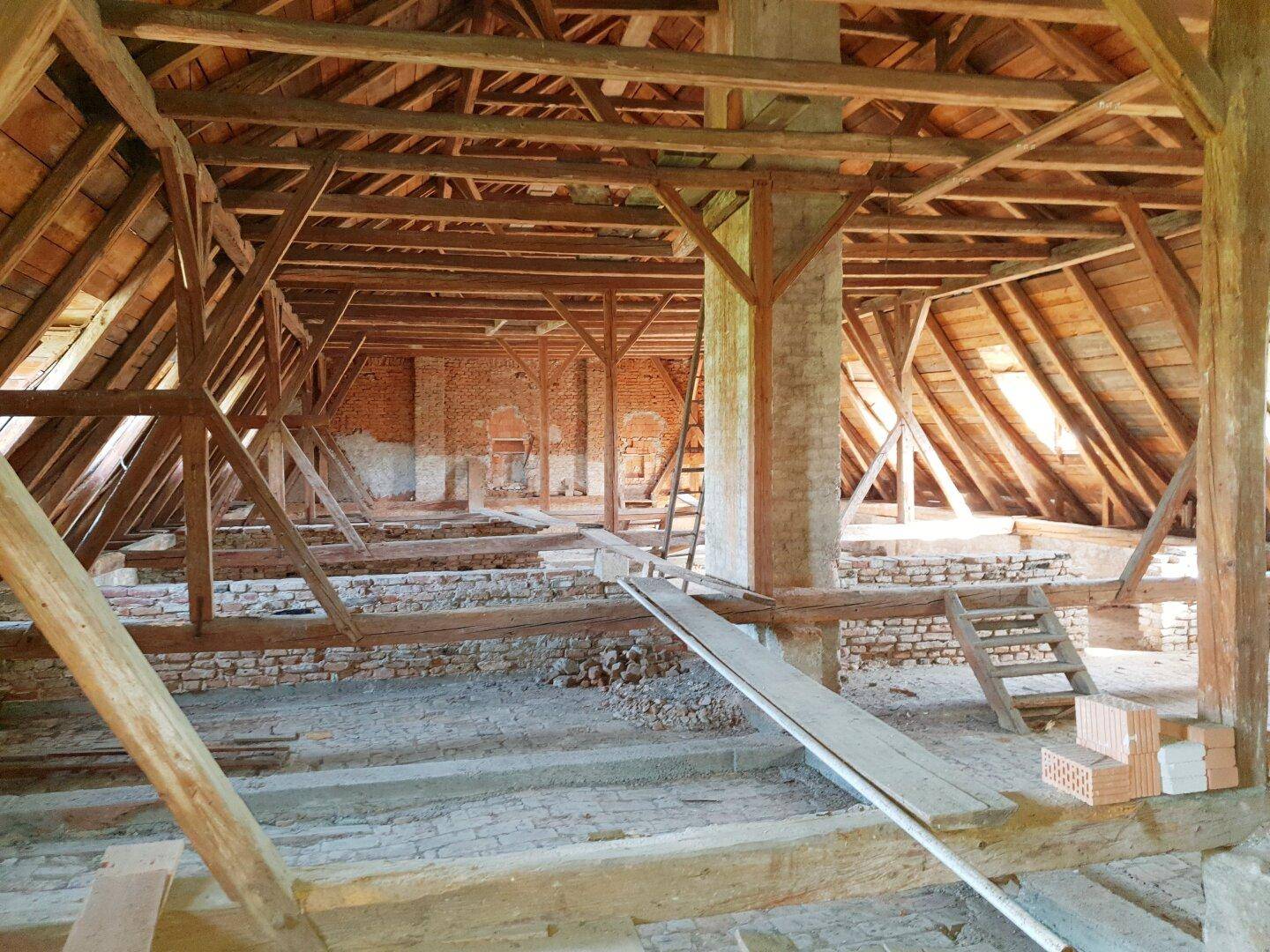 Geräumiger Dachboden mit sichtbaren Holzbalken und Ziegelwänden, bereit für den Ausbau.