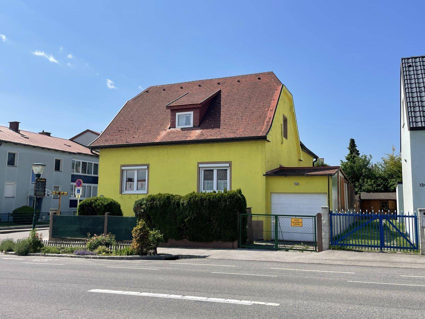 Gelbes Haus mit rotem Ziegeldach und Garage, umgeben von einer Hecke und einem Gartentor.