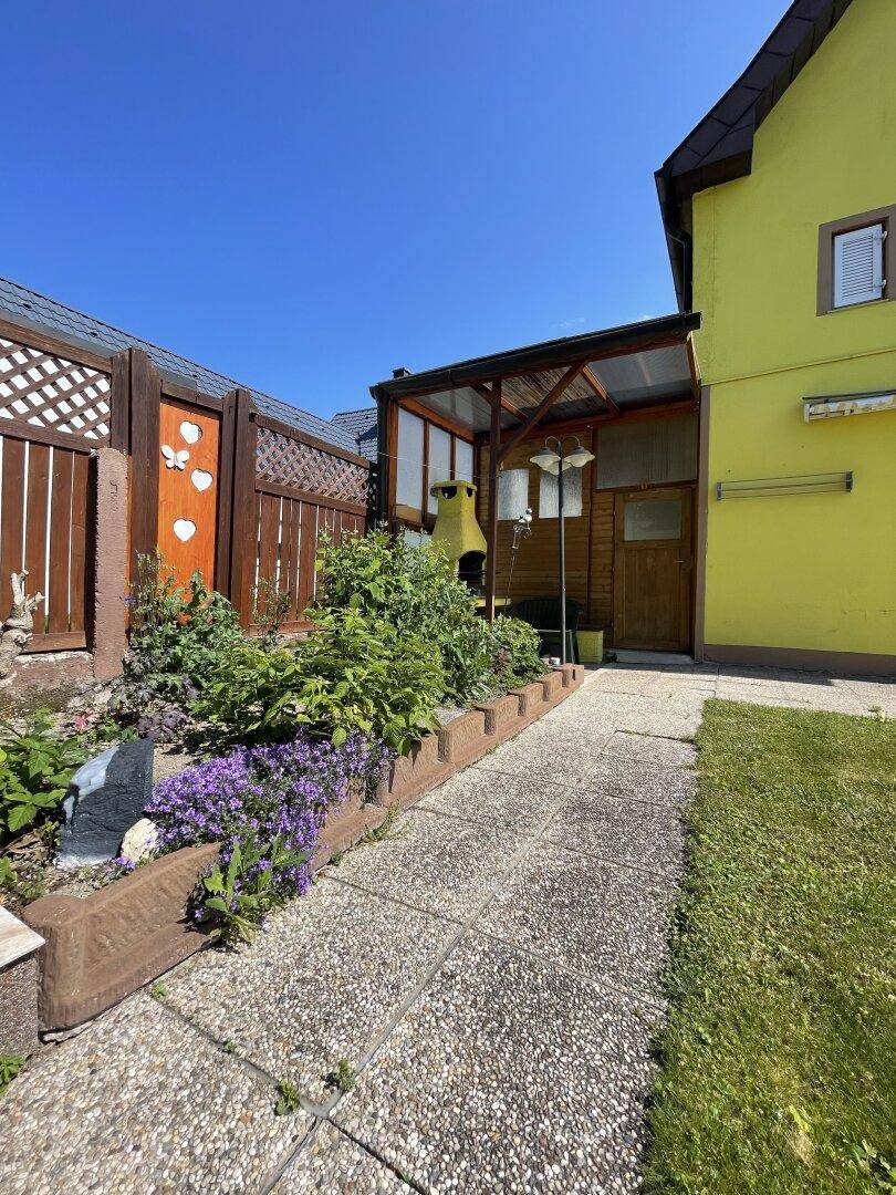 Gartenweg aus Steinplatten führt zu einem überdachten Grillbereich und einem Gartenhaus.