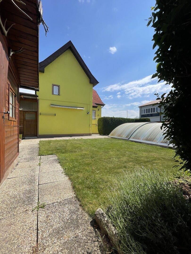 Gartenbereich mit Rasenfläche, Steinplattenweg und einer Abdeckung für einen Pool unter blauem Himmel.
