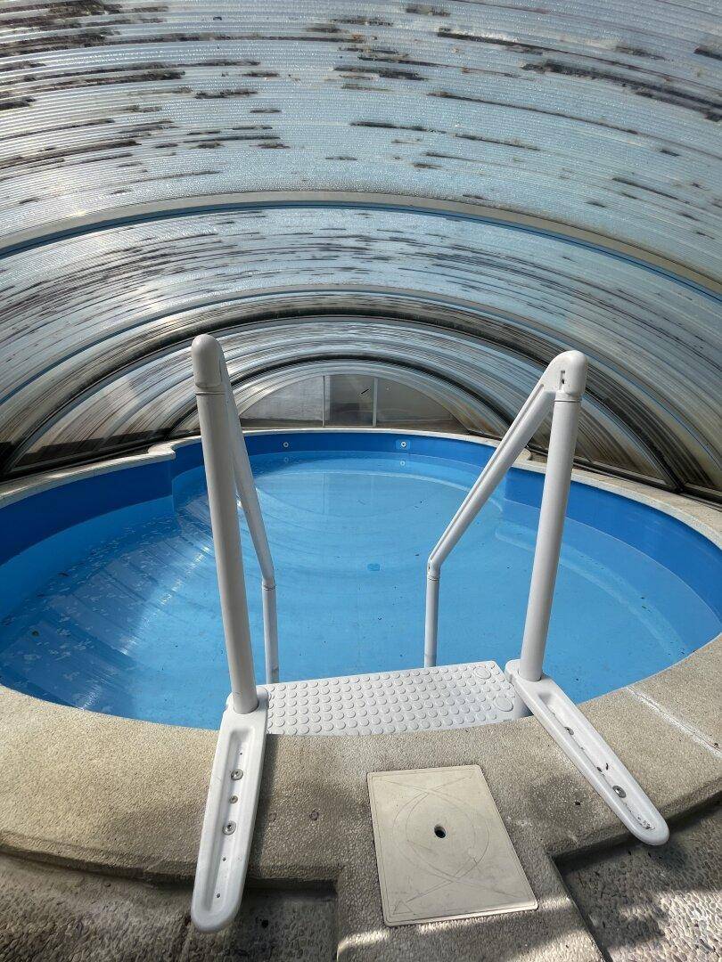 Überdachter runder Pool mit blauer Wasseroberfläche und Einstiegsleiter im Gartenbereich.