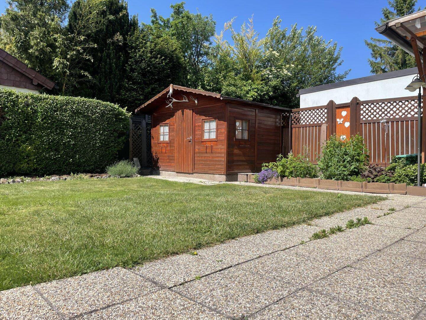 Gepflegter Garten mit Rasenfläche, Steinplattenweg und einem Holzgartenhaus.